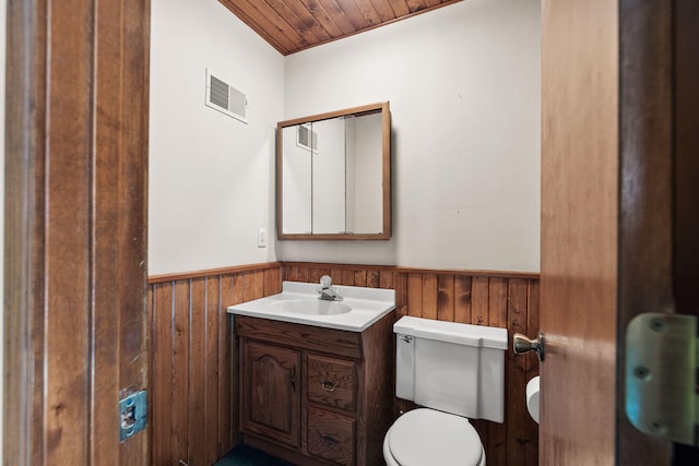 bathroom with vanity, toilet, wooden walls, and wood ceiling