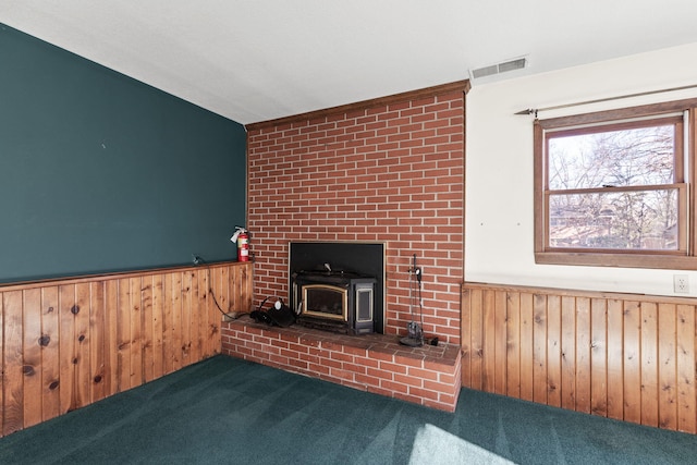 unfurnished living room with a wood stove, dark carpet, and wooden walls