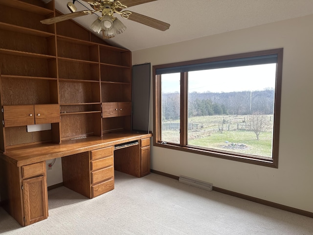 unfurnished office featuring built in desk, light colored carpet, plenty of natural light, and ceiling fan