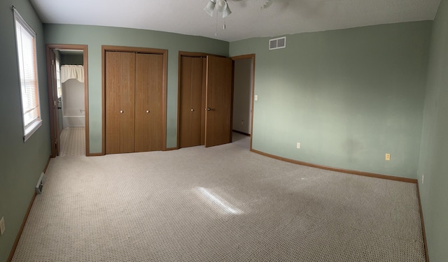 unfurnished bedroom featuring ceiling fan, light colored carpet, and two closets