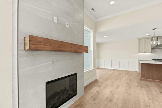 unfurnished living room with visible vents, ornamental molding, light wood-type flooring, wainscoting, and a tiled fireplace