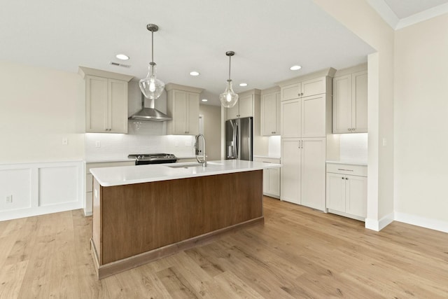 kitchen featuring visible vents, wall chimney exhaust hood, stainless steel appliances, light countertops, and a sink