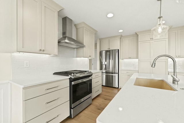 kitchen featuring light wood finished floors, wall chimney exhaust hood, appliances with stainless steel finishes, pendant lighting, and a sink