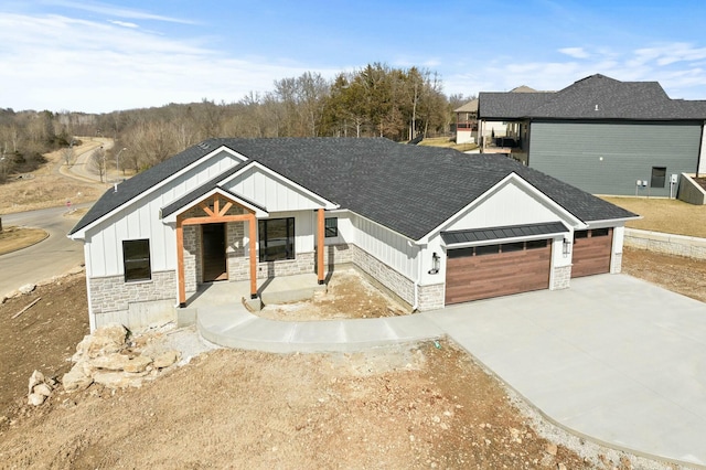 modern farmhouse featuring covered porch, a standing seam roof, a garage, stone siding, and driveway