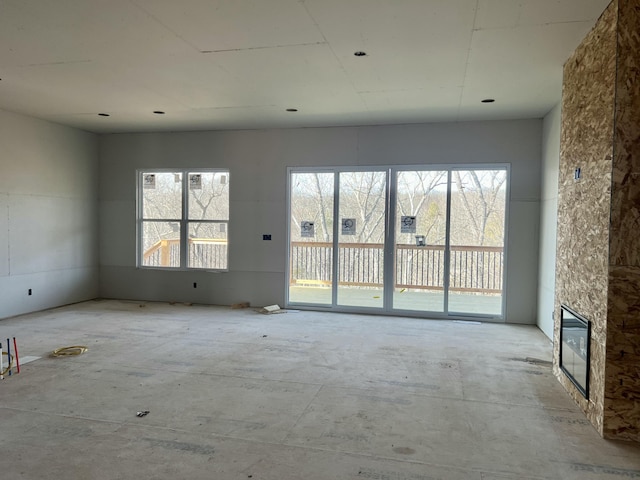 unfurnished living room with plenty of natural light and a stone fireplace