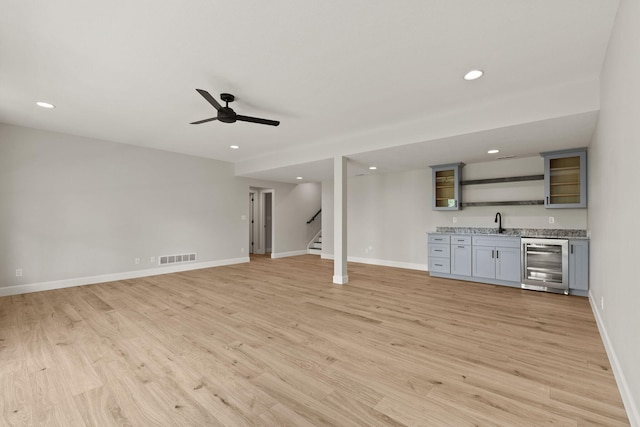 unfurnished living room with ceiling fan, indoor wet bar, stairs, wine cooler, and visible vents