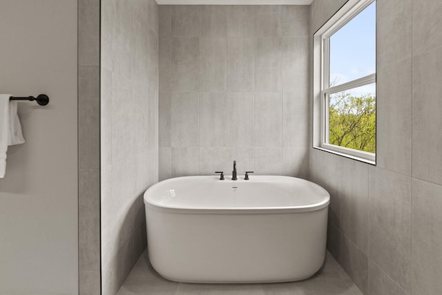 bathroom with a healthy amount of sunlight, tile walls, and a soaking tub
