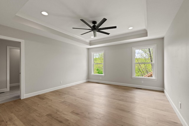 spare room with a ceiling fan, light wood finished floors, and a raised ceiling