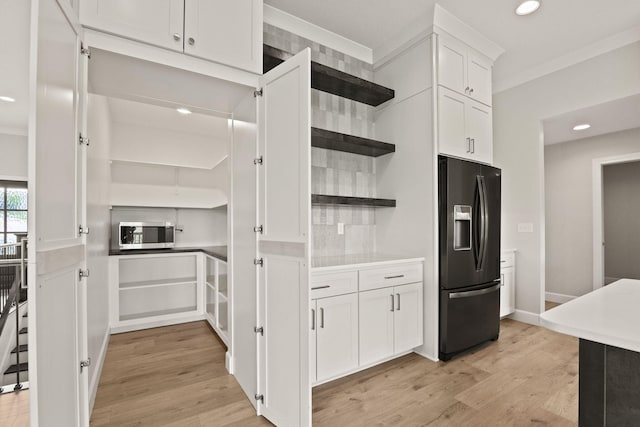 kitchen featuring open shelves, white cabinetry, stainless steel microwave, black fridge, and light wood-style flooring