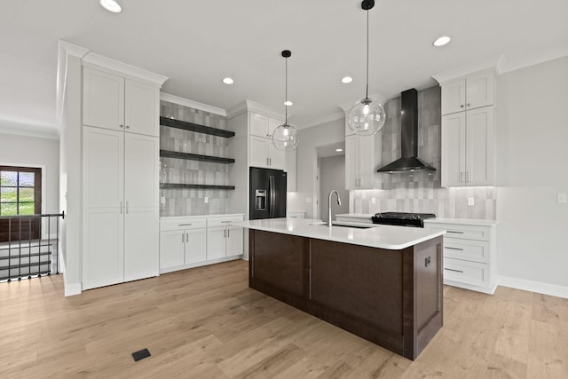 kitchen featuring black fridge with ice dispenser, open shelves, ornamental molding, wall chimney exhaust hood, and a sink