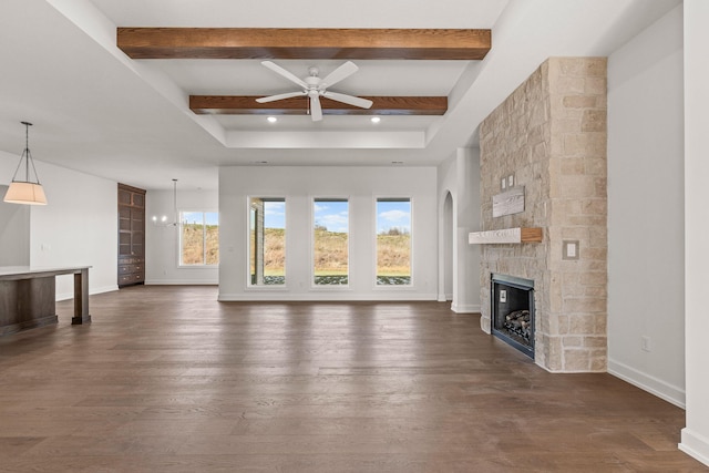 unfurnished living room with a stone fireplace, ceiling fan with notable chandelier, beamed ceiling, and dark hardwood / wood-style floors