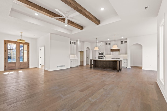 unfurnished living room featuring dark wood-type flooring, french doors, ceiling fan, a tray ceiling, and beamed ceiling