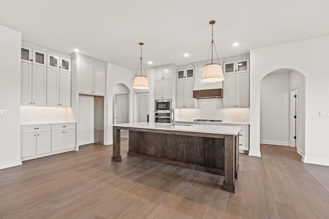 kitchen with a center island with sink, hanging light fixtures, dark wood-type flooring, and appliances with stainless steel finishes