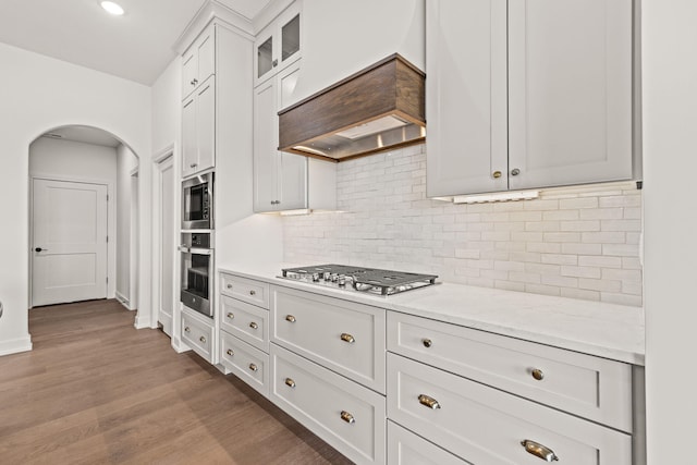 kitchen with white cabinetry, stainless steel appliances, light stone counters, light wood-type flooring, and custom exhaust hood