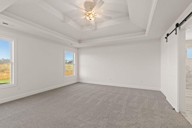 carpeted empty room featuring ceiling fan, a barn door, a wealth of natural light, and a tray ceiling