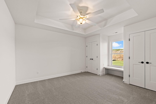 unfurnished bedroom with light colored carpet, a raised ceiling, and ceiling fan