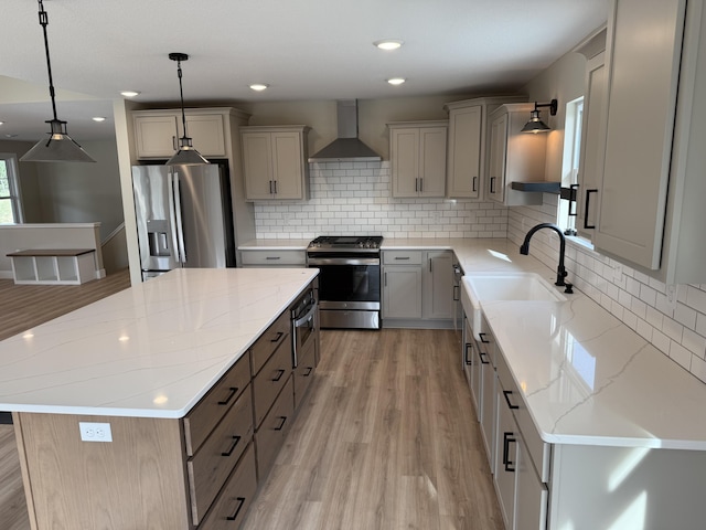 kitchen with hanging light fixtures, wall chimney range hood, light hardwood / wood-style floors, a kitchen island, and appliances with stainless steel finishes