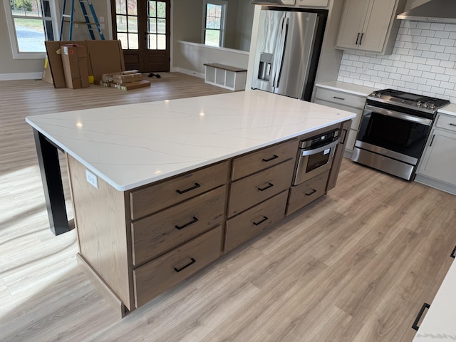 kitchen with a wealth of natural light, light hardwood / wood-style flooring, wall chimney range hood, and appliances with stainless steel finishes