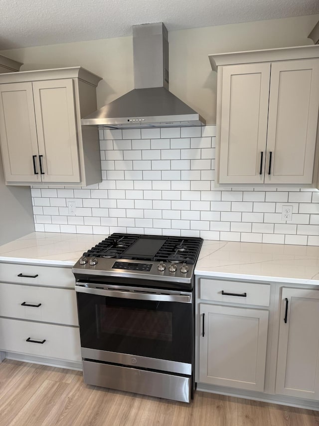 kitchen featuring backsplash, wall chimney range hood, stainless steel gas stove, a textured ceiling, and light hardwood / wood-style floors