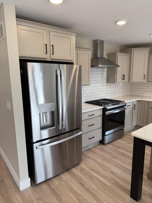 kitchen with appliances with stainless steel finishes, tasteful backsplash, wall chimney range hood, light hardwood / wood-style flooring, and gray cabinets