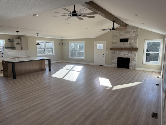 unfurnished living room featuring dark hardwood / wood-style flooring, a textured ceiling, ceiling fan, a fireplace, and vaulted ceiling with beams