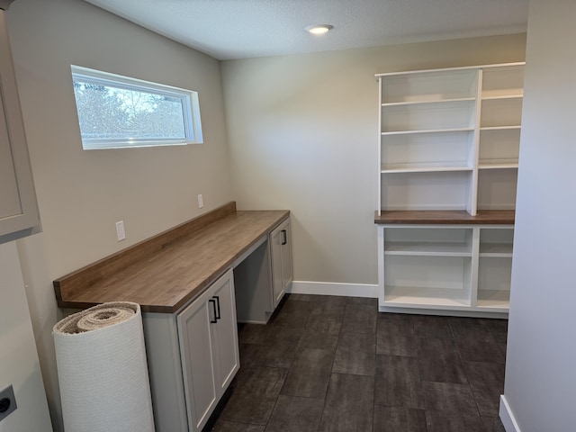 unfurnished office featuring built in desk, dark wood-type flooring, and a textured ceiling