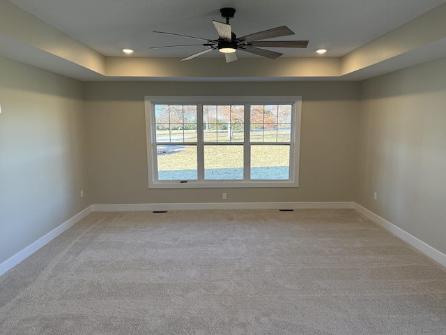 unfurnished room with ceiling fan, light colored carpet, and a tray ceiling