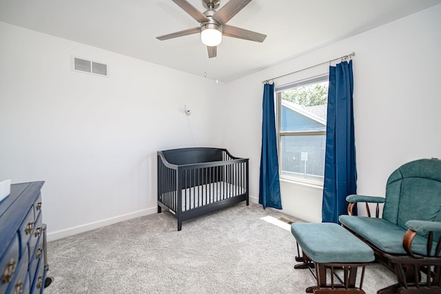 carpeted bedroom featuring ceiling fan and a crib