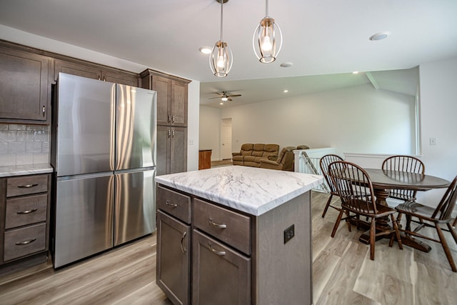 kitchen with pendant lighting, stainless steel fridge, a kitchen island, and light hardwood / wood-style floors