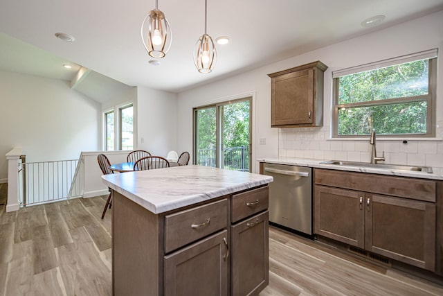 kitchen featuring backsplash, stainless steel dishwasher, sink, pendant lighting, and light hardwood / wood-style flooring