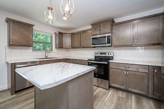 kitchen with sink, hanging light fixtures, stainless steel appliances, light hardwood / wood-style flooring, and a kitchen island