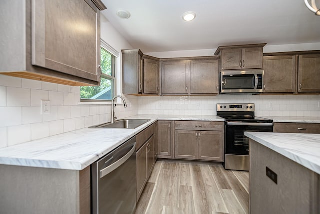 kitchen with sink, light hardwood / wood-style flooring, decorative backsplash, light stone countertops, and stainless steel appliances