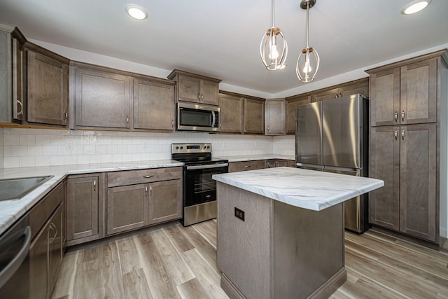 kitchen with decorative backsplash, stainless steel appliances, pendant lighting, light hardwood / wood-style floors, and a kitchen island