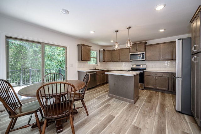 kitchen with stainless steel appliances, sink, light hardwood / wood-style floors, a kitchen island, and hanging light fixtures