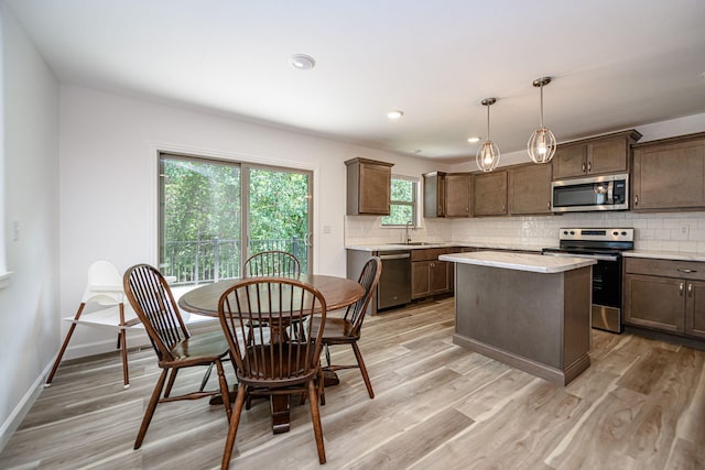 kitchen featuring appliances with stainless steel finishes, sink, decorative light fixtures, light hardwood / wood-style floors, and a kitchen island