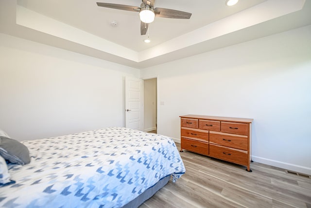 bedroom featuring a raised ceiling, ceiling fan, and light hardwood / wood-style floors