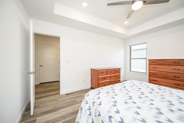 bedroom with ceiling fan, a tray ceiling, and light hardwood / wood-style flooring