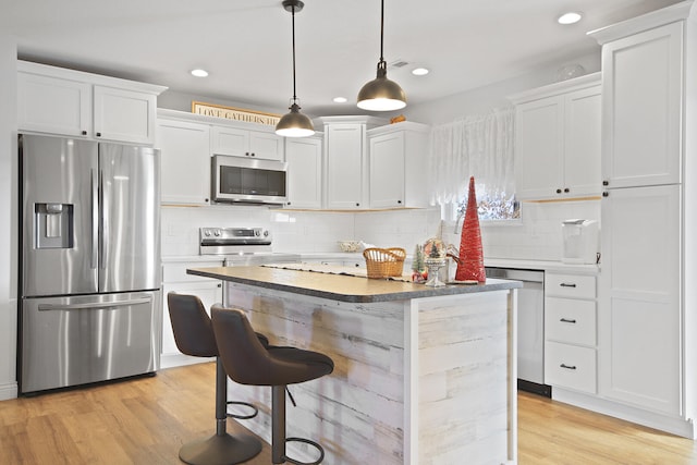 kitchen with light wood-type flooring, stainless steel appliances, pendant lighting, white cabinets, and a center island