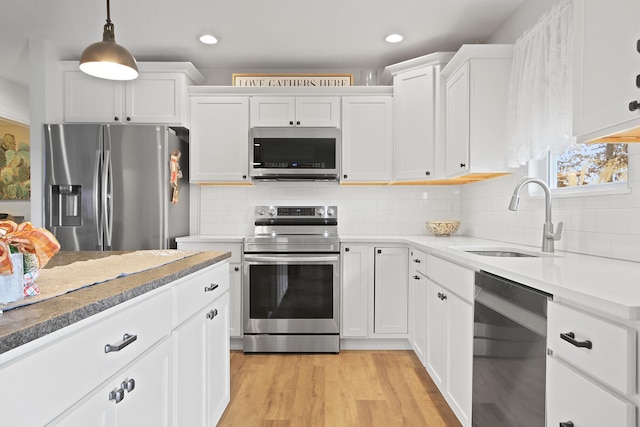 kitchen with sink, stainless steel appliances, pendant lighting, light hardwood / wood-style floors, and white cabinets