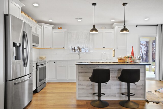 kitchen with a breakfast bar, hanging light fixtures, light wood-type flooring, appliances with stainless steel finishes, and white cabinetry