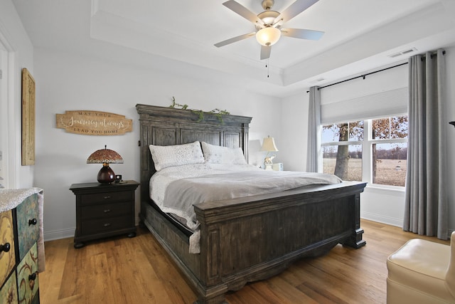 bedroom featuring light wood-type flooring, a tray ceiling, and ceiling fan