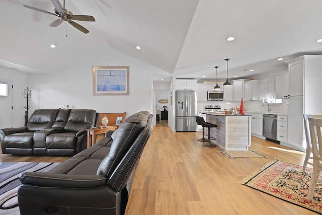 living room featuring ceiling fan, sink, vaulted ceiling, and light wood-type flooring