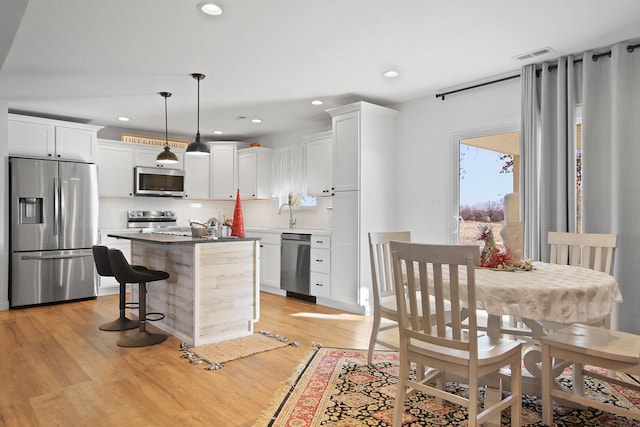 kitchen featuring white cabinets, appliances with stainless steel finishes, decorative light fixtures, and light hardwood / wood-style floors