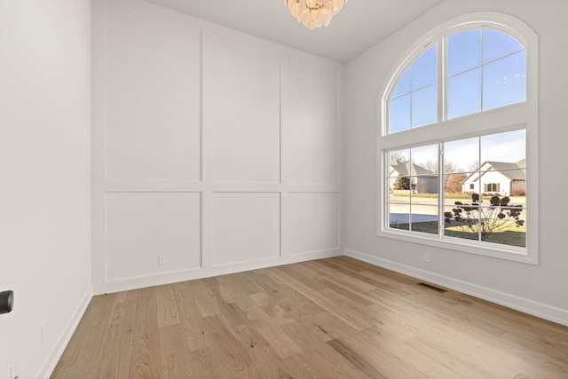 empty room with light wood-type flooring and an inviting chandelier