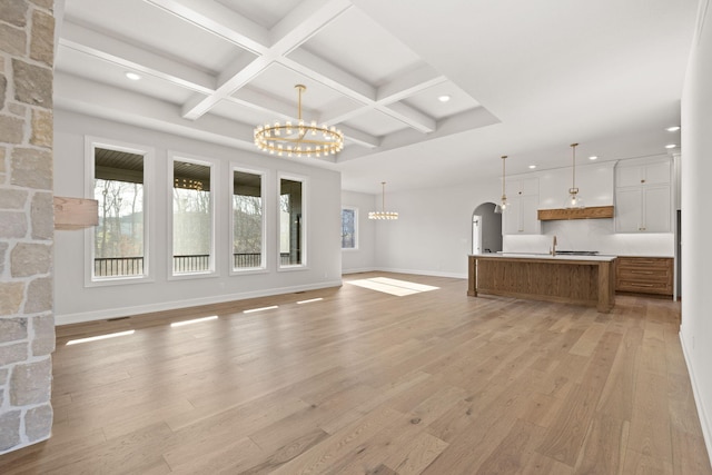 unfurnished living room featuring beamed ceiling, a notable chandelier, light wood-type flooring, and coffered ceiling