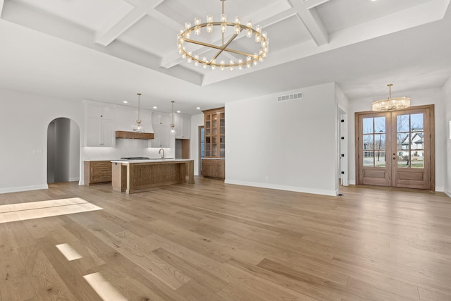 unfurnished living room with french doors, light wood-type flooring, an inviting chandelier, and sink