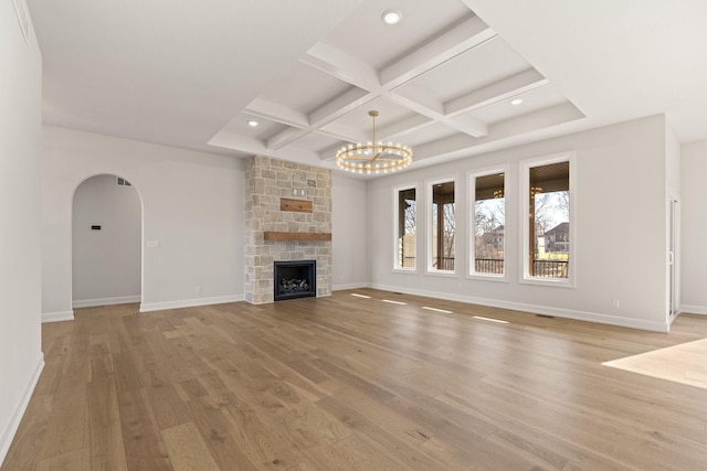 unfurnished living room featuring coffered ceiling, beam ceiling, an inviting chandelier, light hardwood / wood-style floors, and a stone fireplace