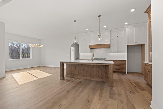 kitchen featuring hanging light fixtures, light hardwood / wood-style floors, decorative backsplash, a center island with sink, and white cabinets