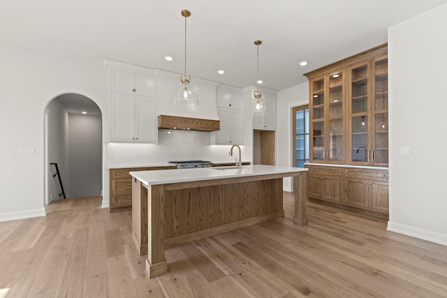 kitchen with a kitchen island with sink, sink, hanging light fixtures, light hardwood / wood-style flooring, and white cabinetry