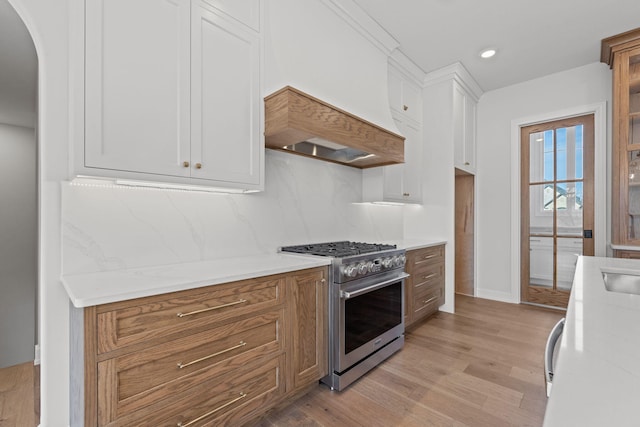 kitchen featuring light stone counters, high end stove, backsplash, light hardwood / wood-style floors, and white cabinets